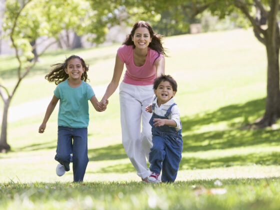 a smiling woman and two young children running hand in hand through an outdoor park