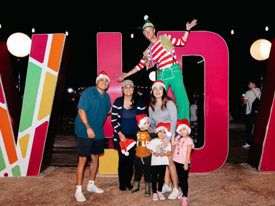 A family wears Santa hat in front of an extra large VIDA sign. Lights of Esperanza, VIDA San Antonio.