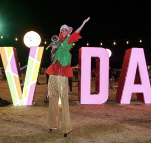 person on stilts in front of lit VIDA sign outdoors