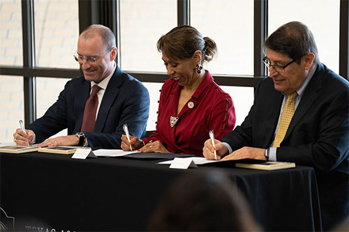 Three people sit and sign paperwork while smiling. University Health, Texas A&M University-San Antonio, Credit: Texas A&M University-San Antonio.