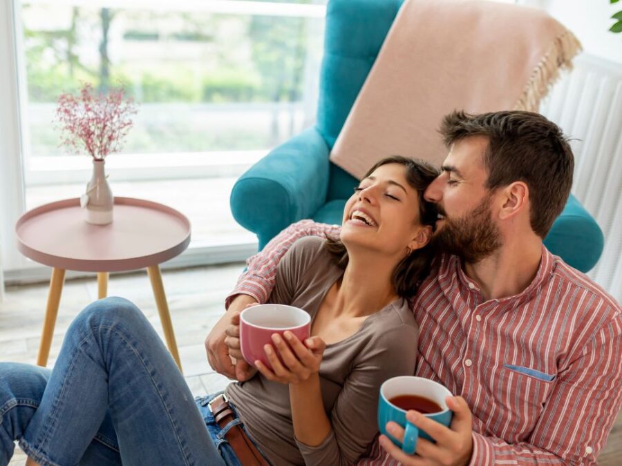 A couple Smile and Drink Tea While Seated on Living Room Floor