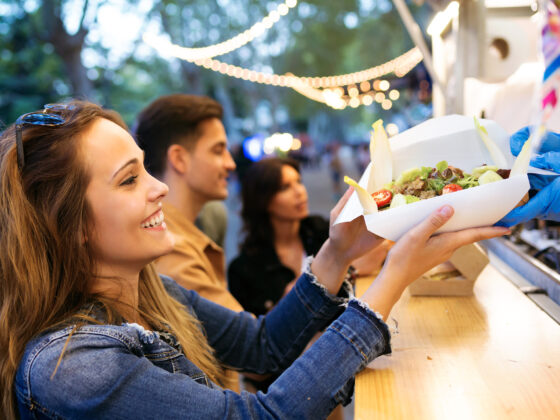 Group of attractive young friends choosing and buying different types of fast food at food trucks in the town center.