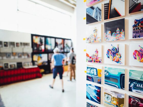 the interior of an an art gallery with multiple pieces of art on the wall, and two people in the background looking at art.