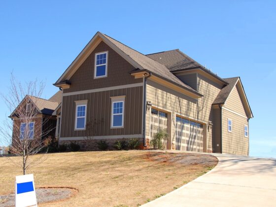 a home with brown siding and three windows facing front and a for sale sign in the front of the house