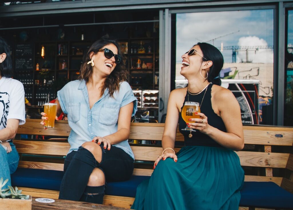 Two stylish friends laugh and enjoy a beer outside of a food truck.