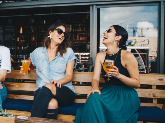 Two stylish friends laugh and enjoy a beer outside of a food truck.