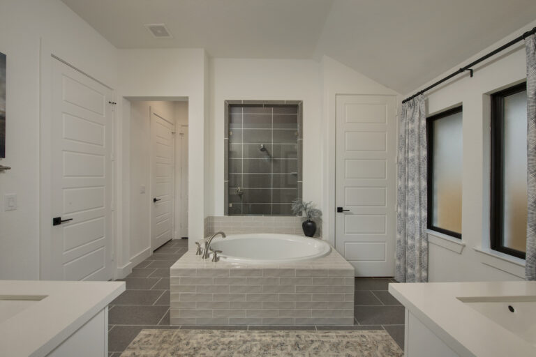A standalone bathtub featured in the Master Bath of a Perry Home, a neutral warm white palette and tiled details