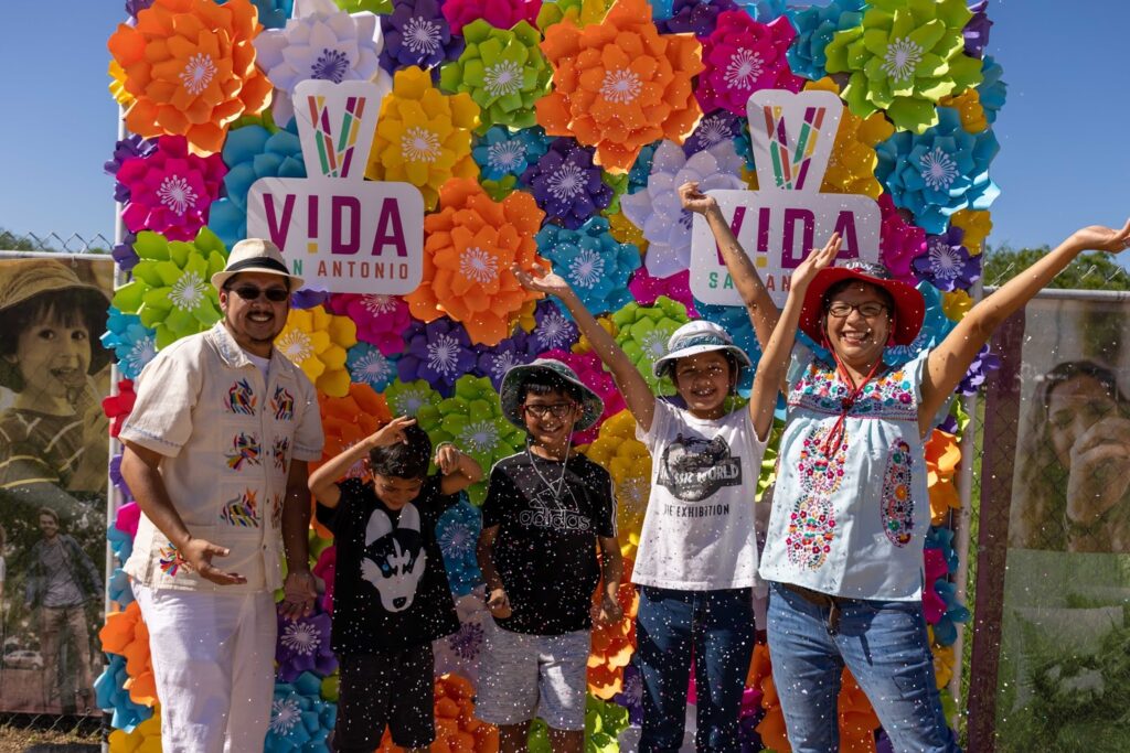 A Latino family cracks a cascarone and throws their arms up at Festival de Cascarones