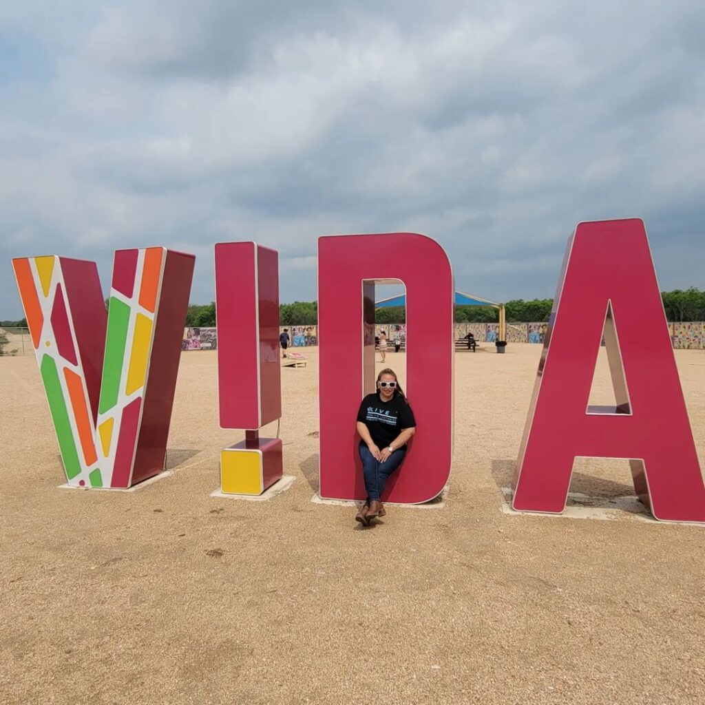 Live From the Southside's April Monterrosa poses at VIDA San Antonio against a giant backdrop of the word "VIDA"