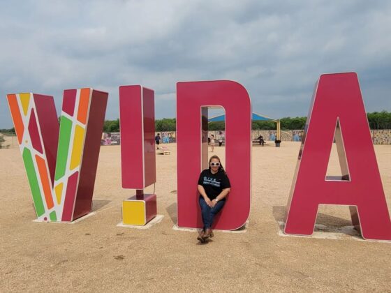 Live From the Southside's April Monterrosa poses at VIDA San Antonio against a giant backdrop of the word "VIDA"