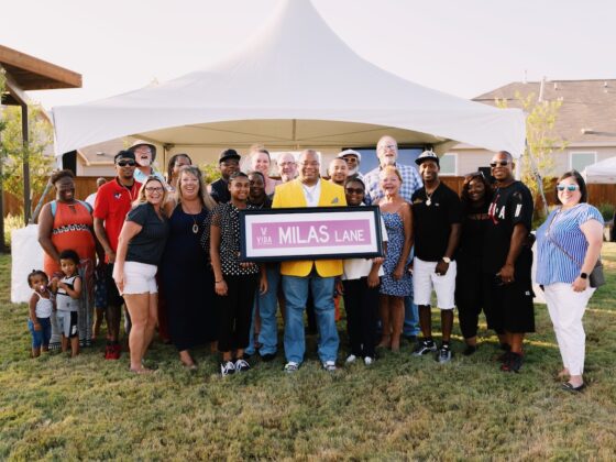 Chef Milas and community members pose for a group photo at sunset outside while he holds a sign that says "Milas Lane"