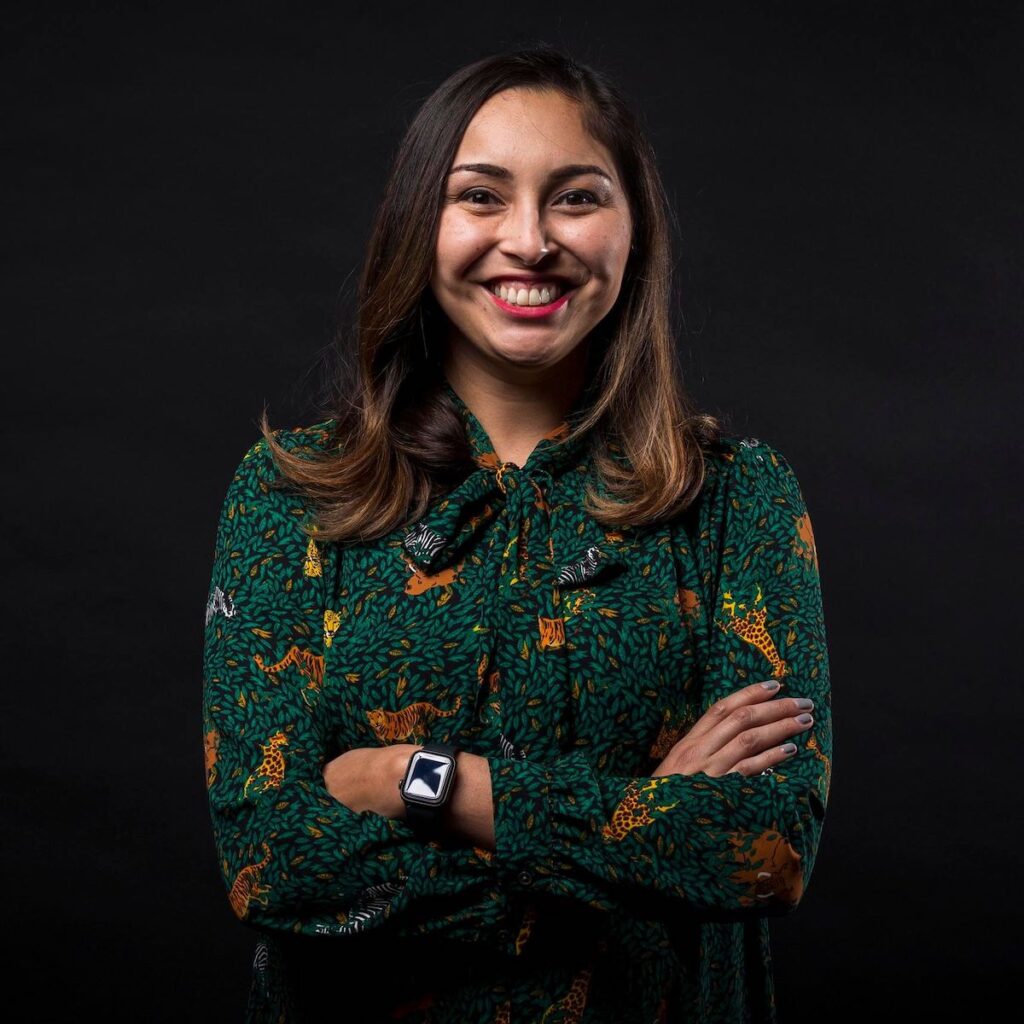 Sara Briseño Gerrish poses in a green blouse with a smile and her arms crossed for a portrait