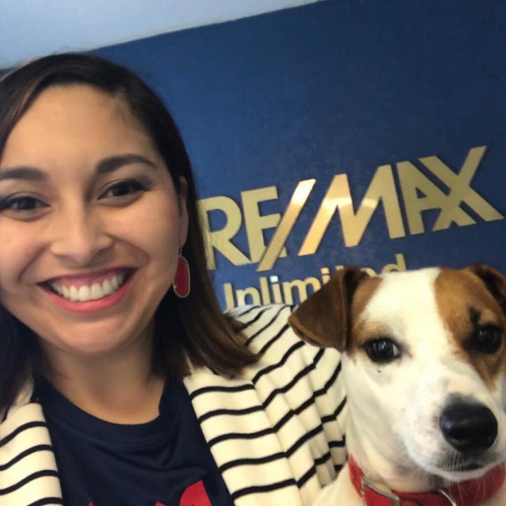 Sara Briseño Gerrish takes a selfie with a small dog in front of the Re/Max sign