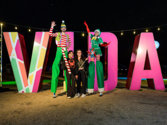 A family poses with festive stilt walkers in front of the VIDA sign