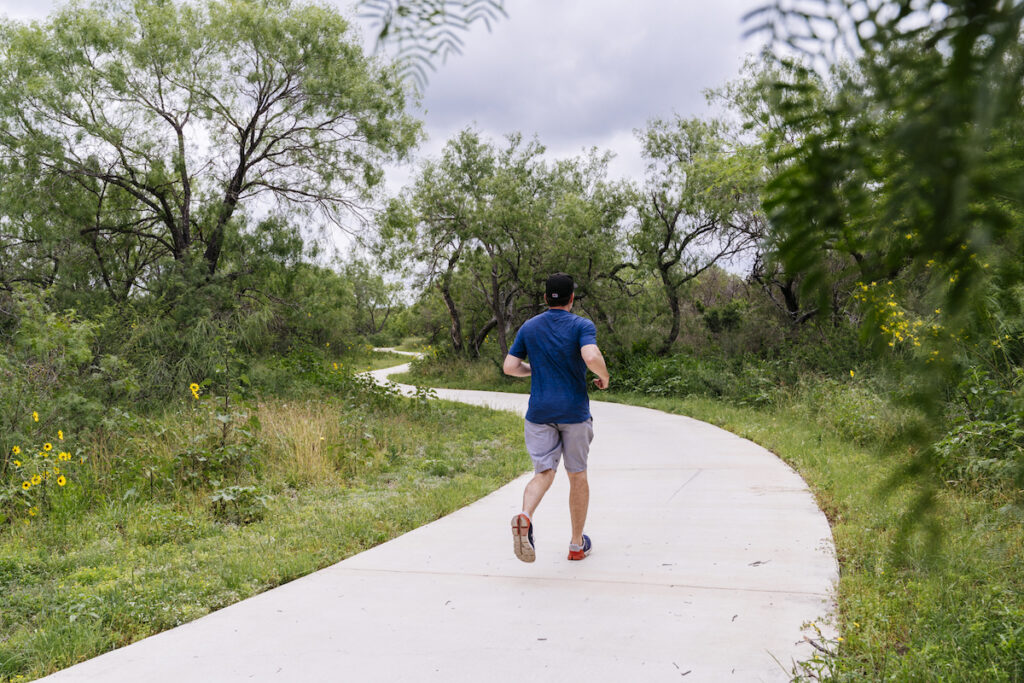 A man runs on a lush trail.