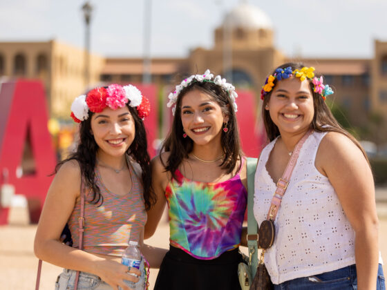 Three women with flower crowns stand in front of Texas A&M San Antonio while attending Festival de Cascarones.