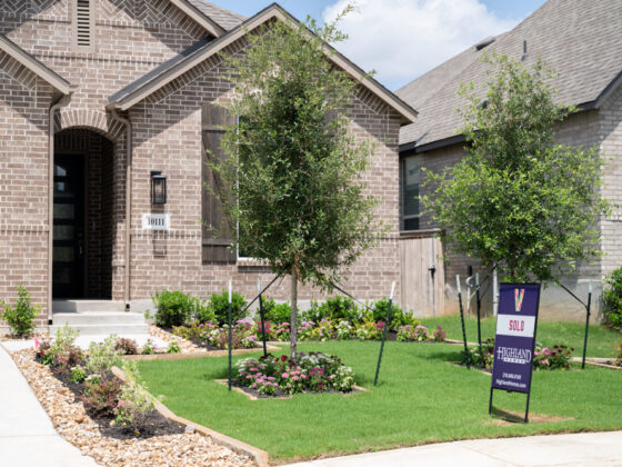 A "Sold" sign sits in the front lawn of a newly built brick Highland home with a lush front yard.
