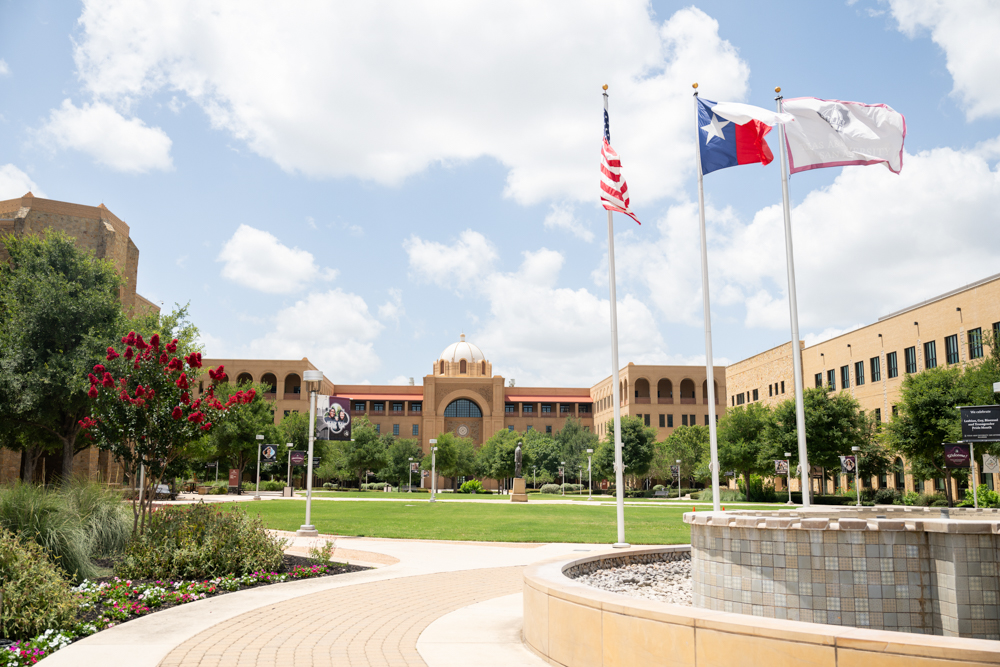 The American flag, the Texas Flag, and the Texas A&M flag stand waving in front of the Texas A&M San Antonio campus