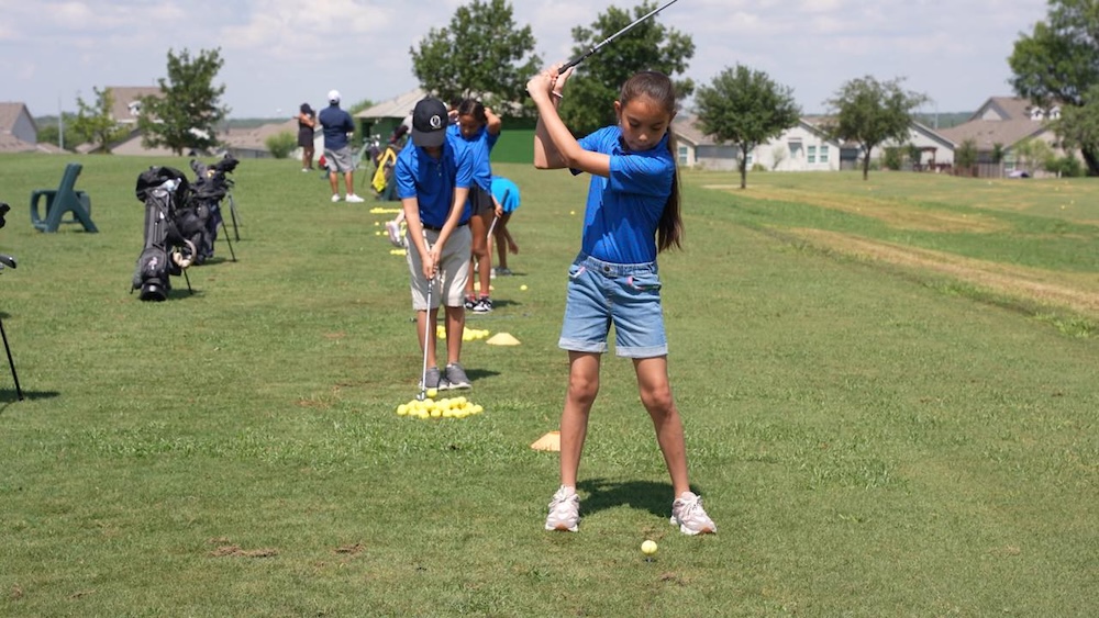 Several youth hit golf balls on a golf course