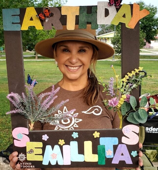 Josie Gutierrez holds up an oversized frame reading, "Earth Day Semillitas"