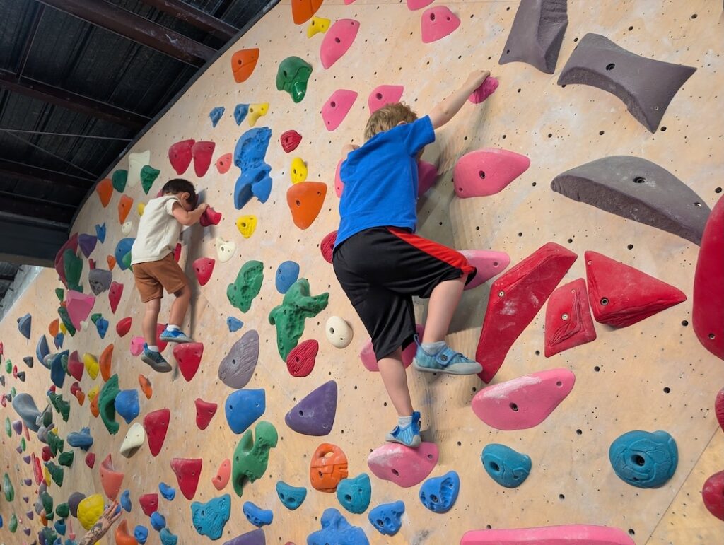Young children rock climb on a colorful wall