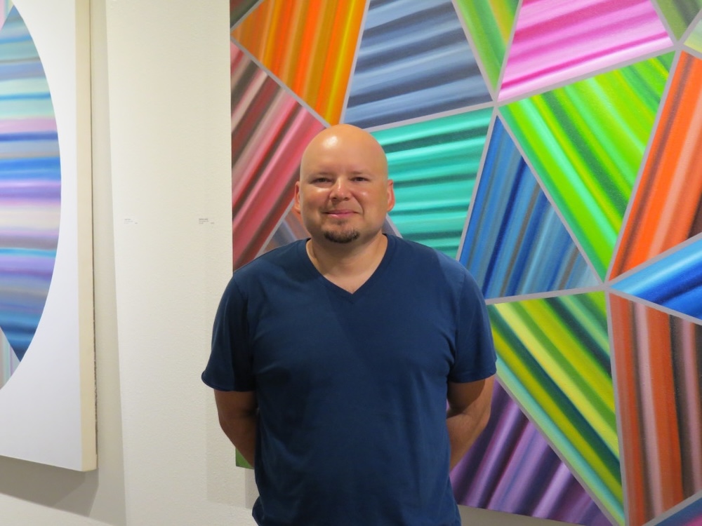 Louis Vega Treviño standing in front of his own artwork displayed in a gallery