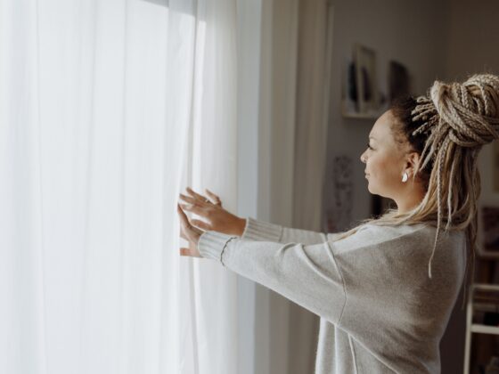 Side view of a woman in loungewear opening curtains to let in morning light.