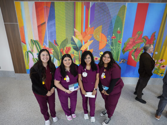 Four University Health Vida clinic staff members stand in purple scrubs smiling in front of colorful mural wall inside the University Health Vida clinic