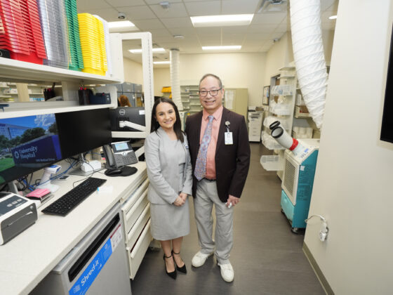 University Health Vida pharmacy staff, a man and woman, stand next to a computer and rows of medication