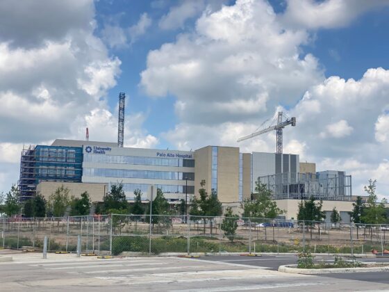 Large cranes are visible around the University Health Palo Alto Hospital, with the exterior completed