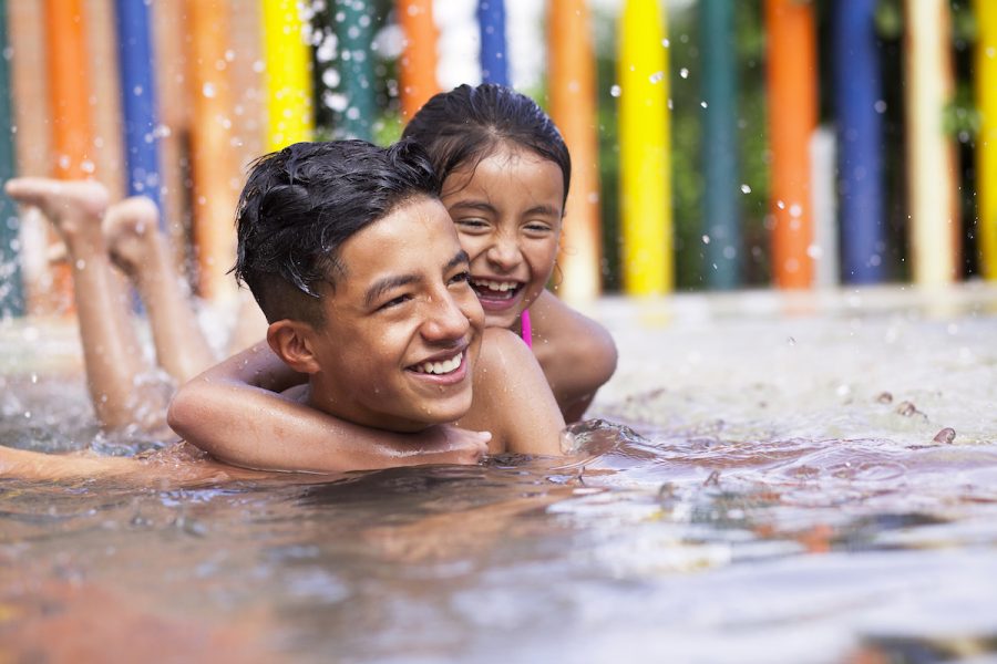 Latino children a teenage boy and an 8-year-old girl play in the pool, cuddle and cuddle in the water while smiling and having fun