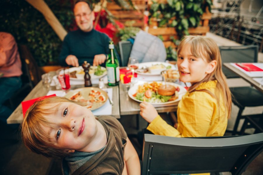 Happy family eating hamburger with french fries and pizza at outdoor restaurant in town center.