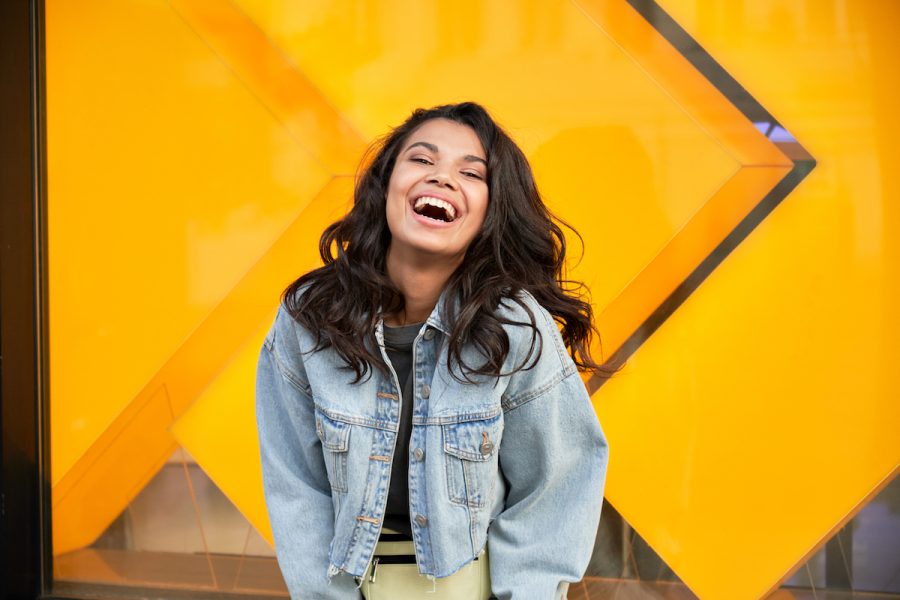 Happy African American woman wearing denim jacket laughing looking at camera standing near city street building. Smiling positive mixed race generation z hipster lady posing outdoor.