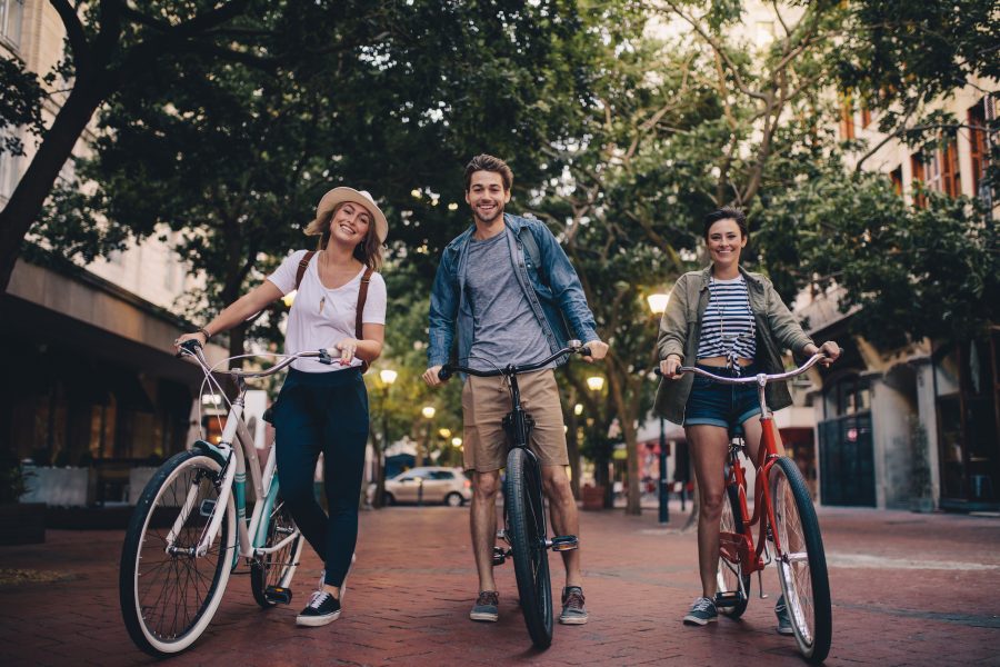 Full length of three young people with their bicycles on city street. Friends on bike ride through the town center.