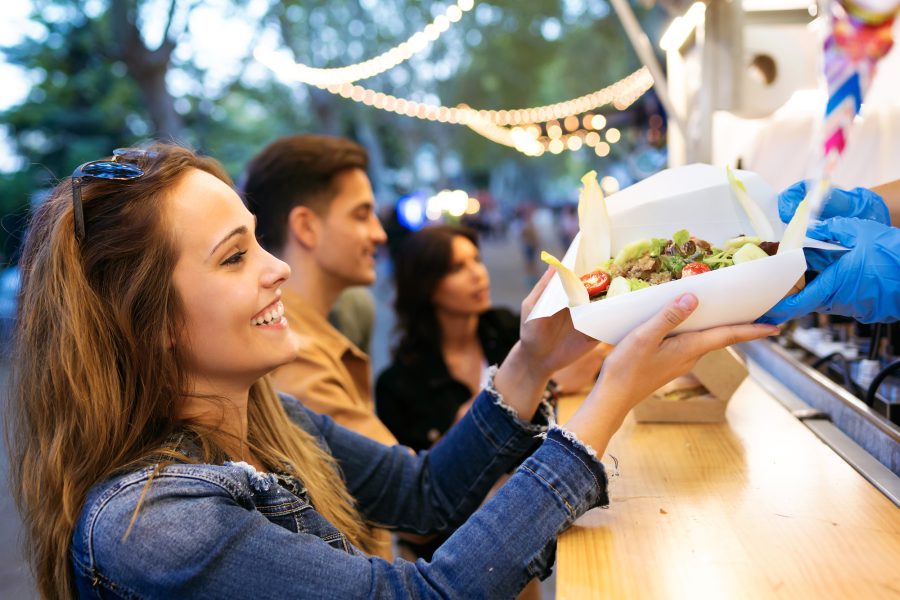 Group of attractive young friends choosing and buying different types of fast food at food trucks in the town center.