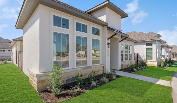 A corner view of a brand new VIDA San Antonio townhome by Sitterle with tall windows and a green front lawn.